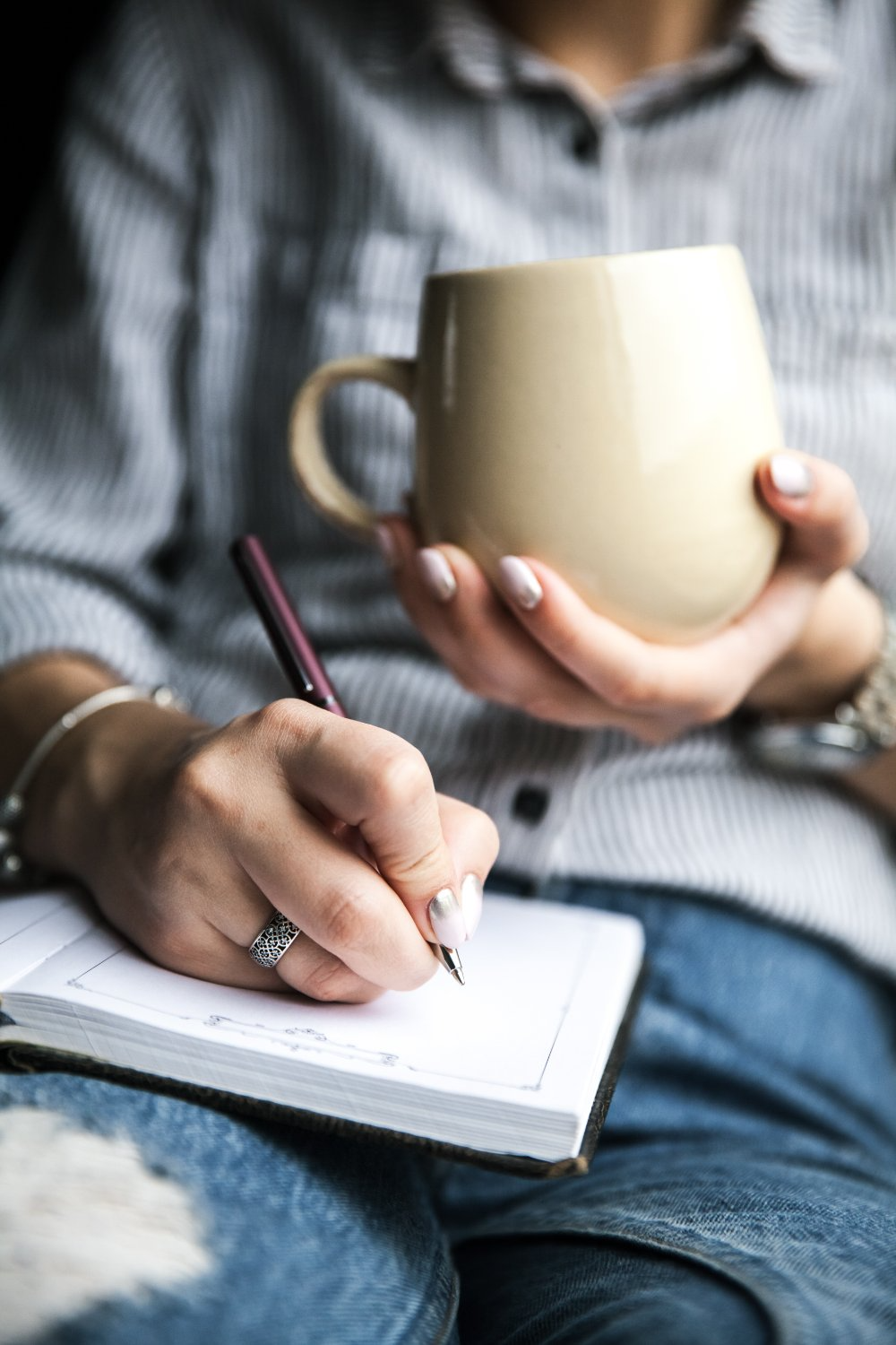Hands holding a warm mug while writing in a notebook