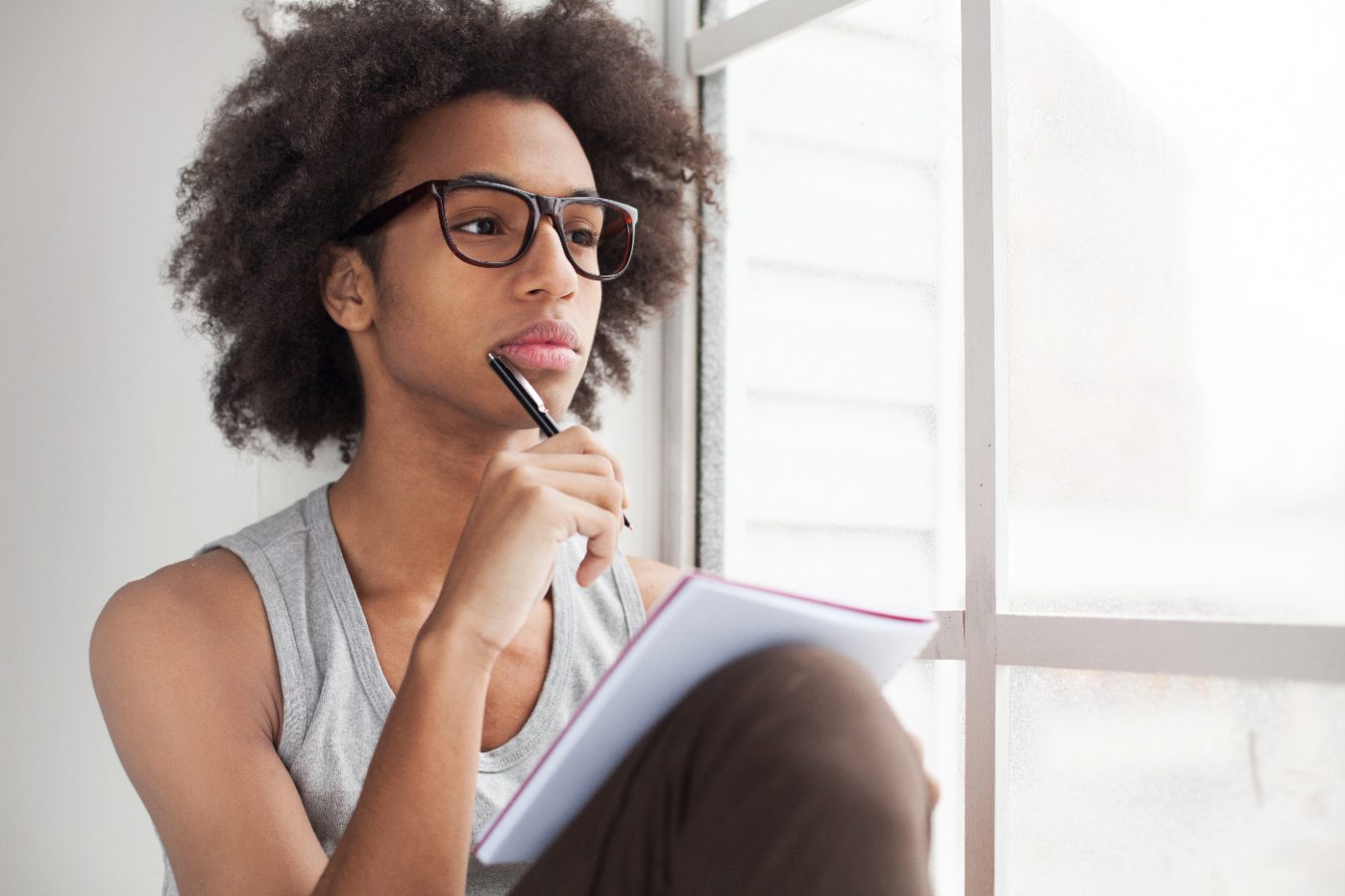 A young person by a window, pen to chin, deep in thought